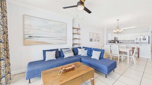 A living room with a blue sofa, a wooden coffee table, and a ceiling fan. - Sunset Tides 1208-Gulf Front Balcony-Sleeps 6 (Panama City Beach)