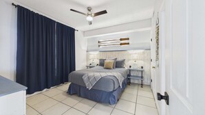 Une chambre à coucher avec un lit, des tables de chevet, un ventilateur de plafond et une vue sur l’extérieur.