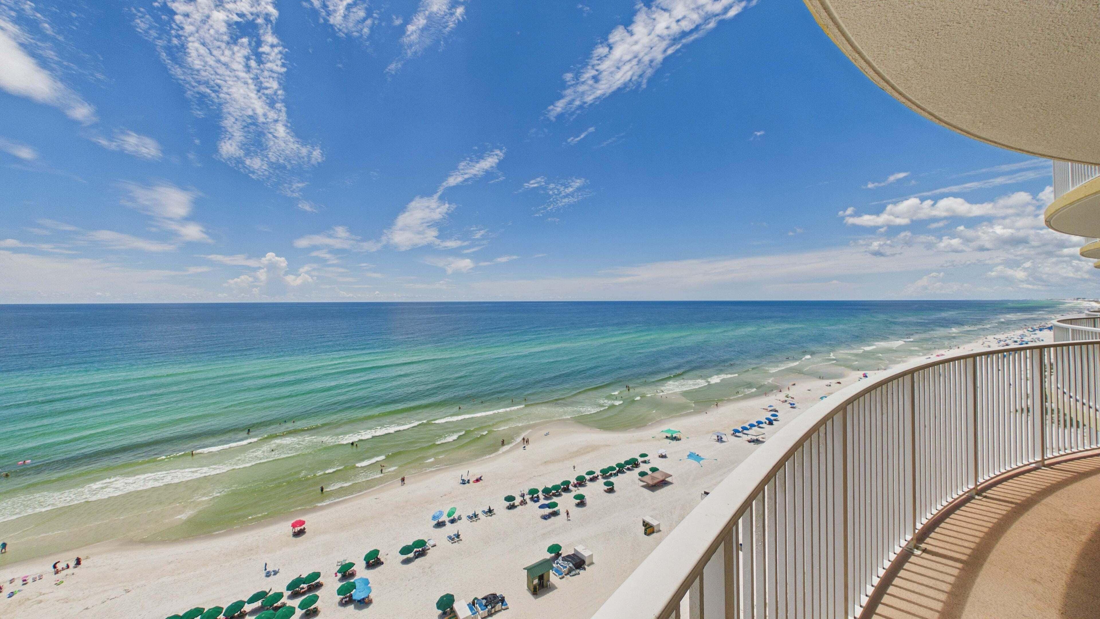 A beach view from a balcony with a railing, clear blue sky, and ocean.