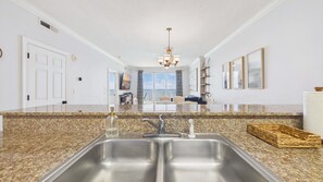 A kitchen with granite countertops, stainless steel sinks, a chandelier, and a view to the outside. - Sunset Tides 1208-Gulf Front Balcony-Sleeps 6 (Panama City Beach)