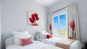 A hotel room with two beds, a window with curtains, and a painting of red flowers on the wall. - El Gouna luxury apartment lagoon and pool view (Red Sea Governorate)