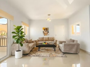 A modern living room with a beige sofa set, a coffee table, a potted plant, and a painting on the wall. - El Gouna luxury apartment lagoon and pool view (Red Sea Governorate)