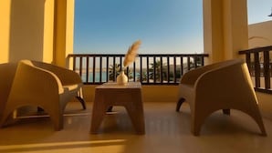 A balcony with wicker furniture, a small table, and a vase with dried plants. - El Gouna luxury apartment lagoon and pool view (Red Sea Governorate)