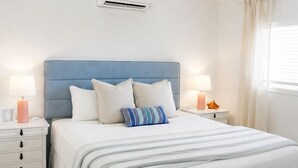 Une chambre à coucher avec un lit, des tables de chevet, un ventilateur de plafond et une fenêtre avec des rideaux.