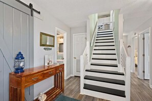 A staircase with a white and black design, a wooden console table with drawers, a blue lantern, and a mirror on the wall. - 418 - Nags Head Sound-side retreat with hot tub! (Nags Head)