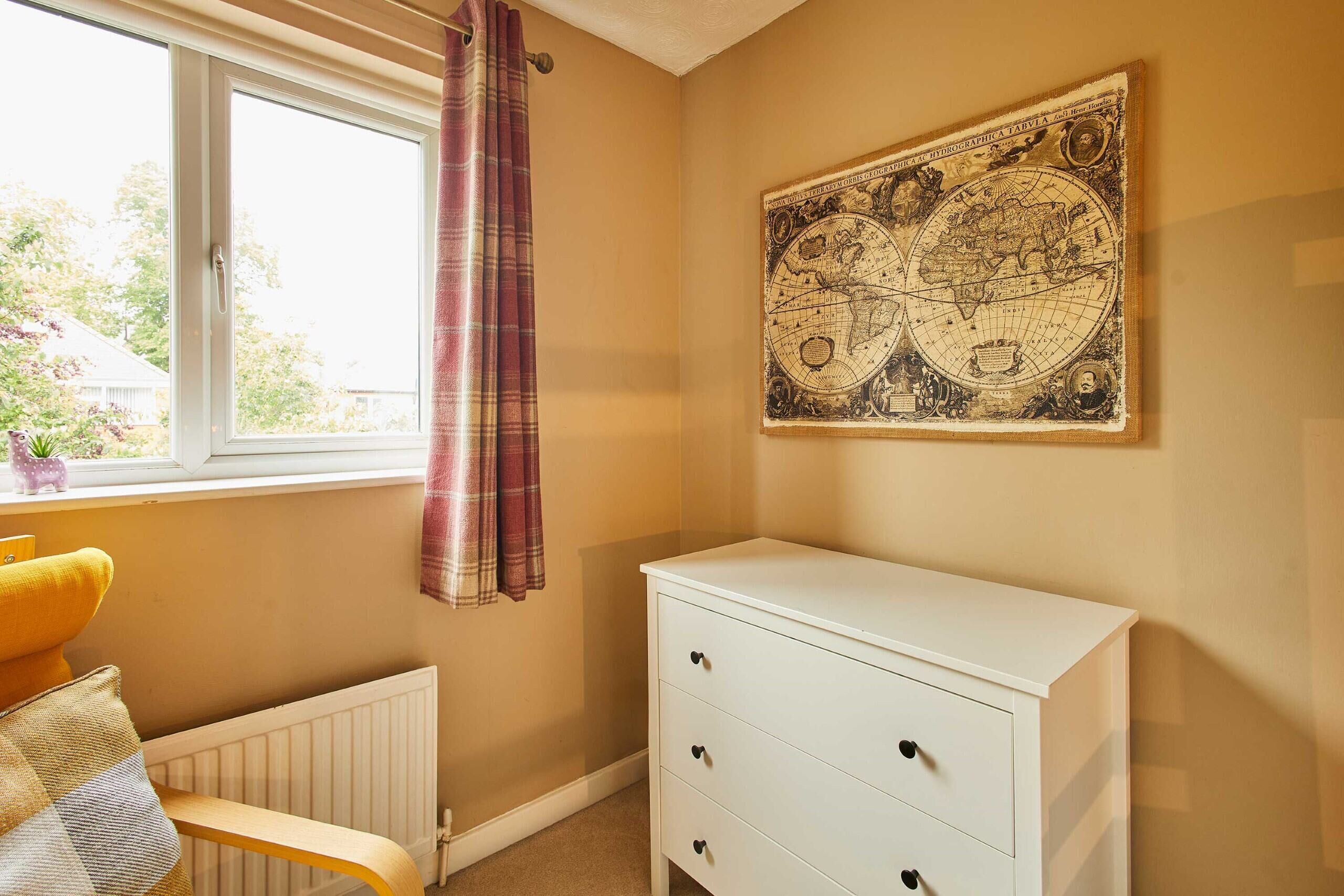 A room with a white dresser, a window with a curtain, and a map on the wall.