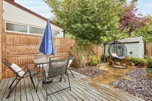 Eine Holzterrasse mit Tisch und Stühlen, einem Hängesessel, einem Gartenbereich mit Blumentöpfen und einem Schuppen.