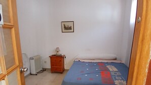 A bedroom with a bed, a radiator, a wooden dresser, and a wall-mounted picture.