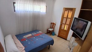 A room with a bed, a television, a chair, and a door.