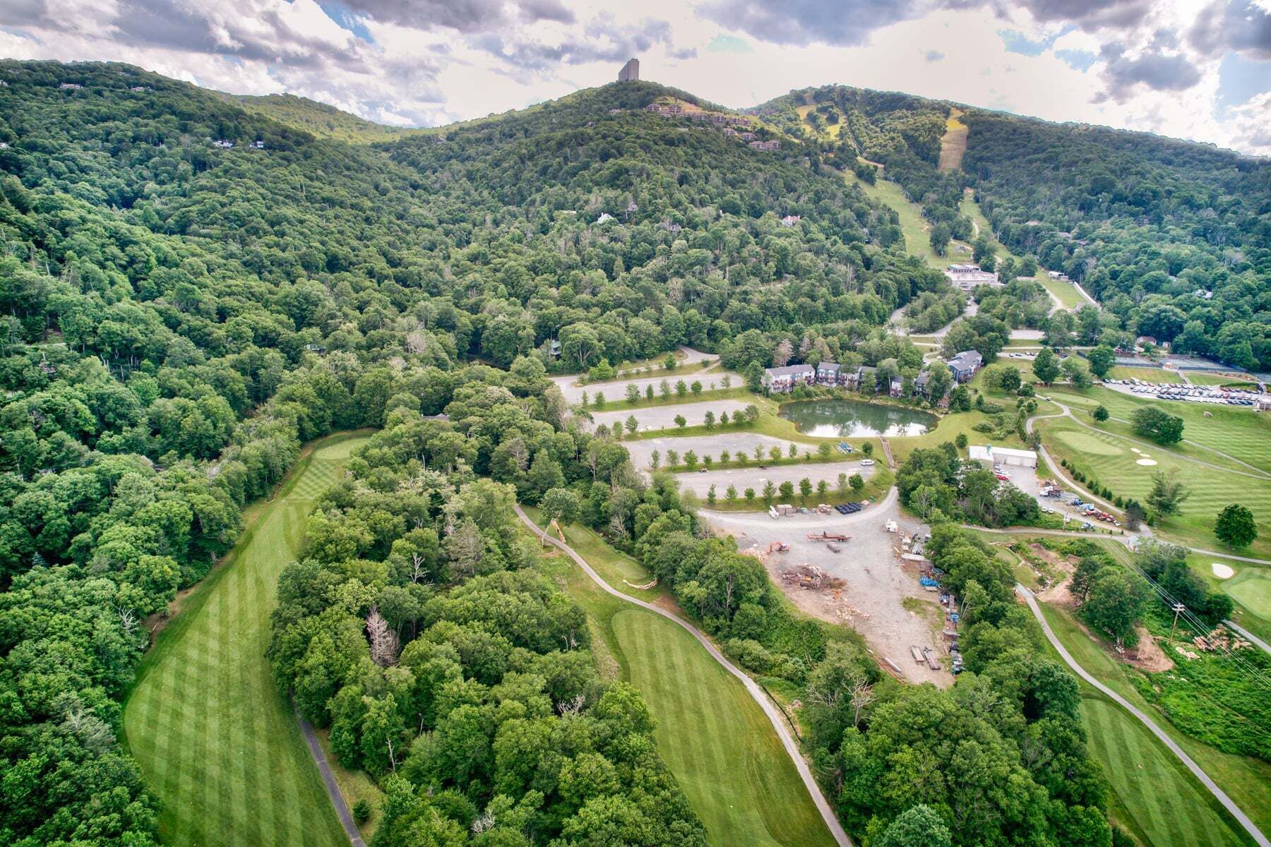 Vue aérienne d’un parcours de golf avec plusieurs greens, un étang et des collines boisées environnantes.