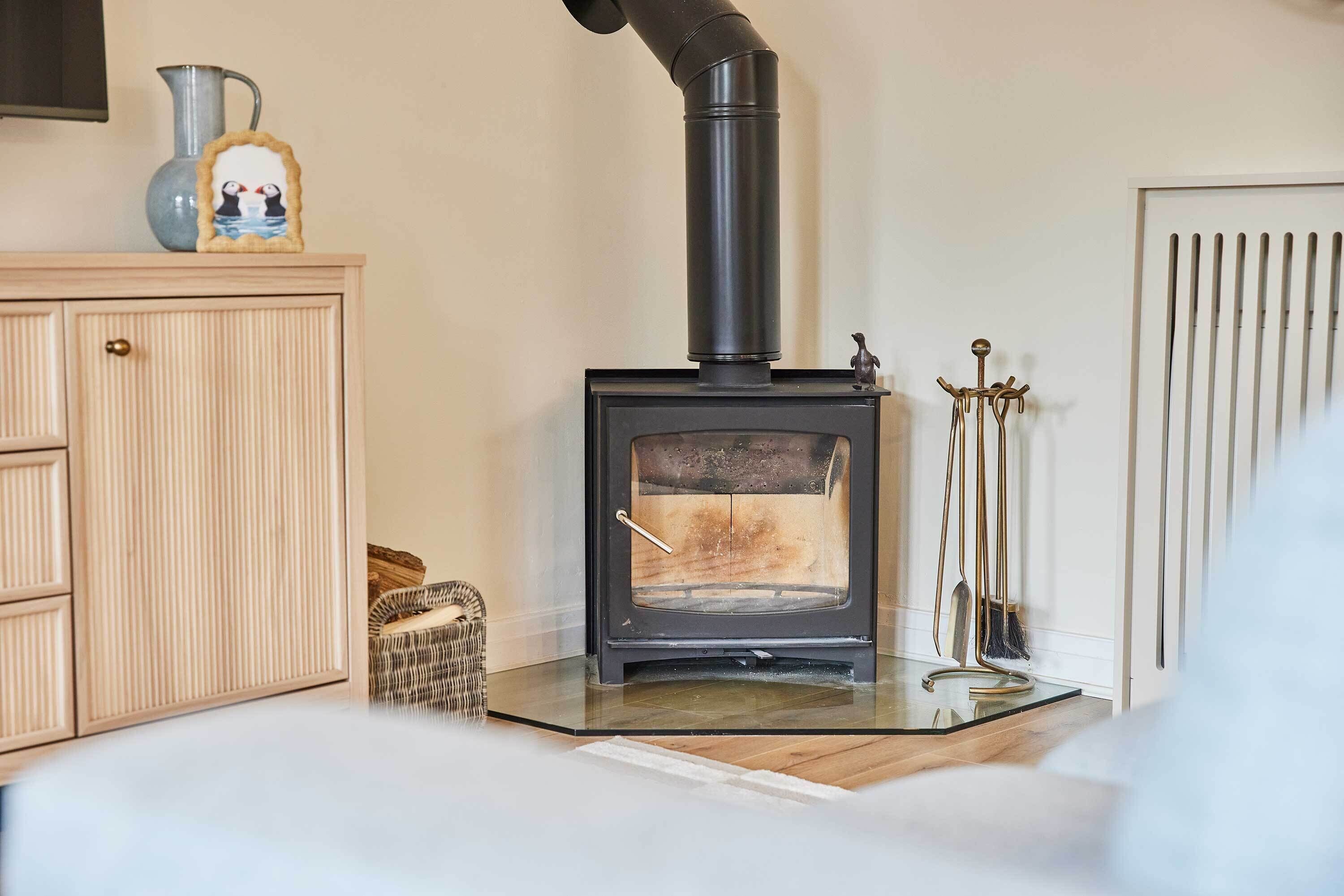 En vedeldad kamin med en skorsten, ett skåp med en bilderam och en kvast som står lutad mot väggen.