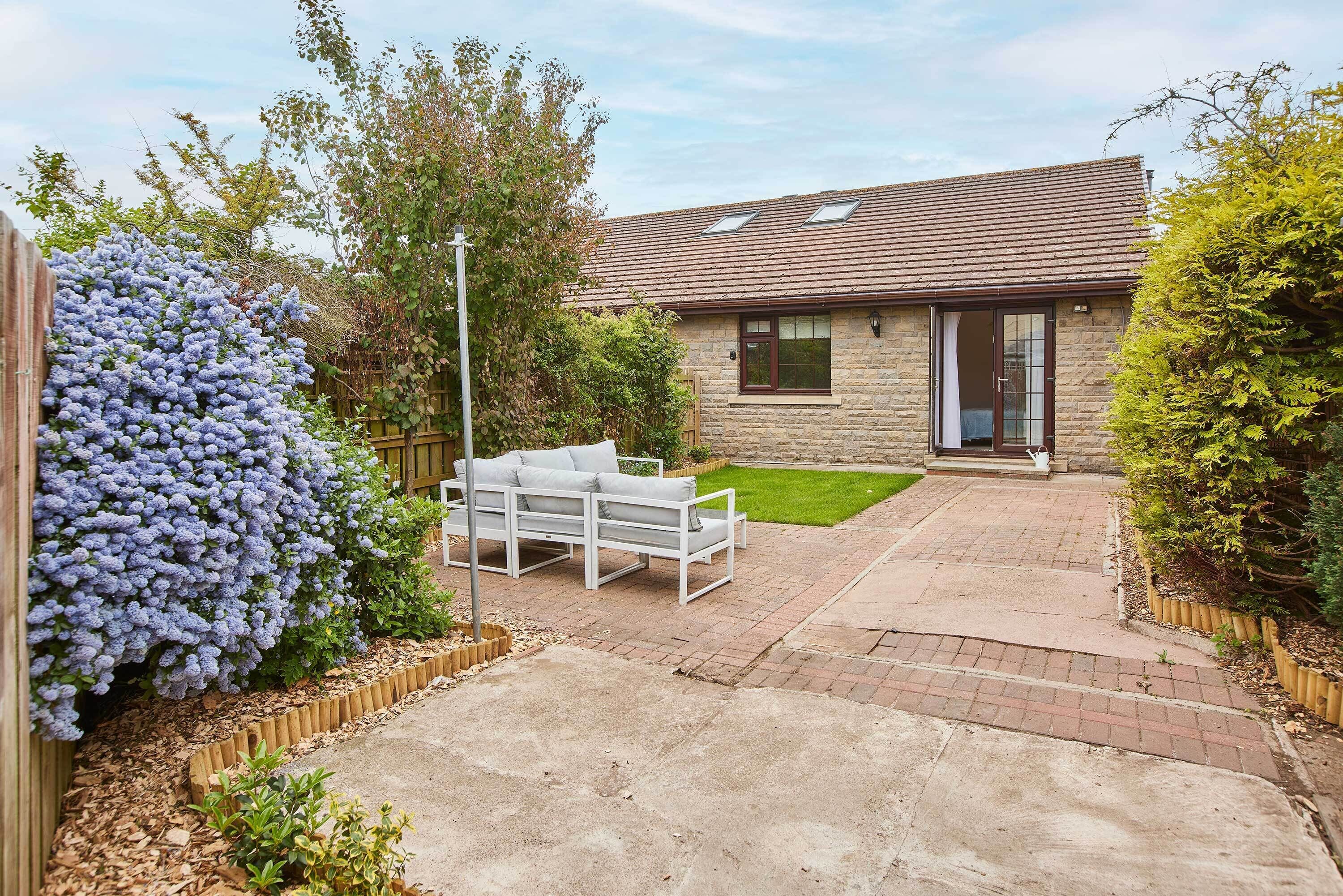 Une maison dotée d’un patio dallé, d’un espace extérieur aménagé avec des meubles blancs et d’un jardin bien entretenu.