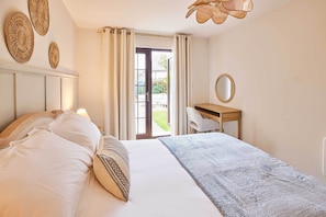 Ein Schlafzimmer mit Bett, Schreibtisch, Stuhl, Spiegel und Blick ins Freie.