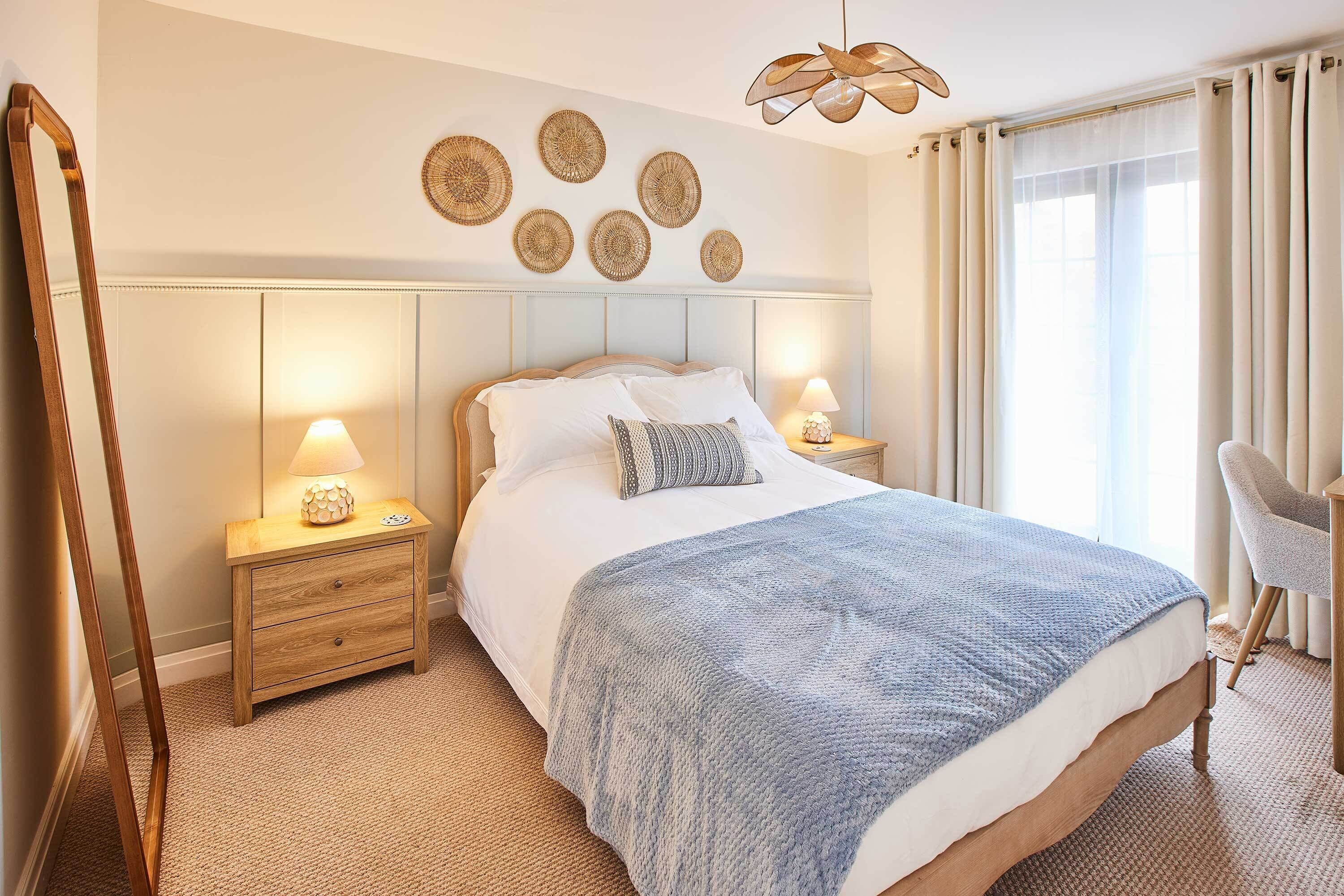 Een keurig opgemaakt slaapkamer met een bed, nachtlampjes, een stoel en decoratie aan de muur.