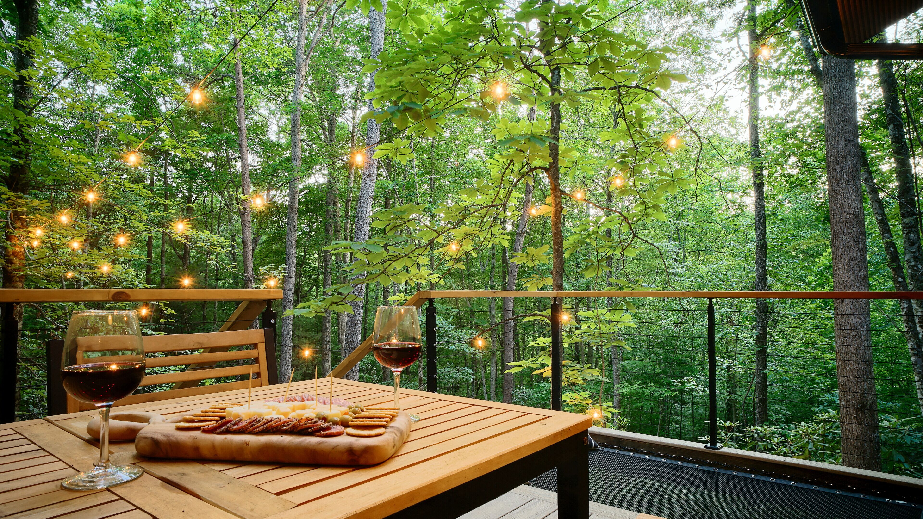A wooden deck with a table set for a meal, surrounded by a forest.