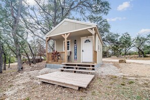 A small cabin with a porch, a welcome sign, and a wooden deck. - Hill Country Cabin 2 (Canyon Lake)