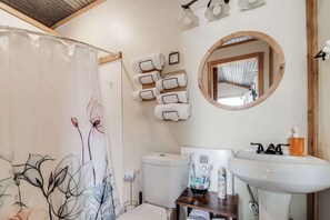 Een badkamer met douchegordijn, toilet, wastafel met spiegel en handdoeken op een rek.