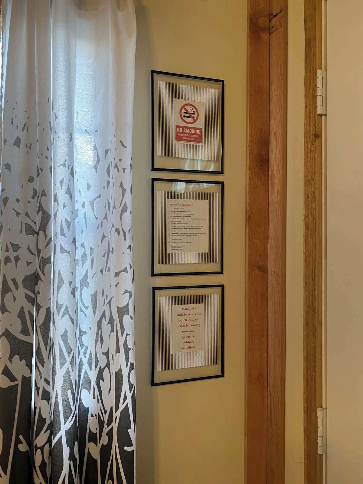 A room with a wooden door, a white curtain with a leaf pattern, and three framed signs on the wall.