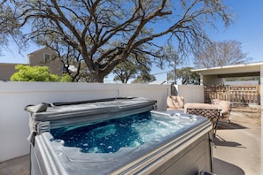 Een hottub met een houten terras, een grote boom en een overdekte patio.