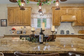 Une cuisine avec des meubles en bois, un plan de travail en granit, une bouteille de vin et des bougies.