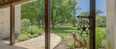 A covered patio with stone flooring, wooden beams, and a view of a grassy area with trees.