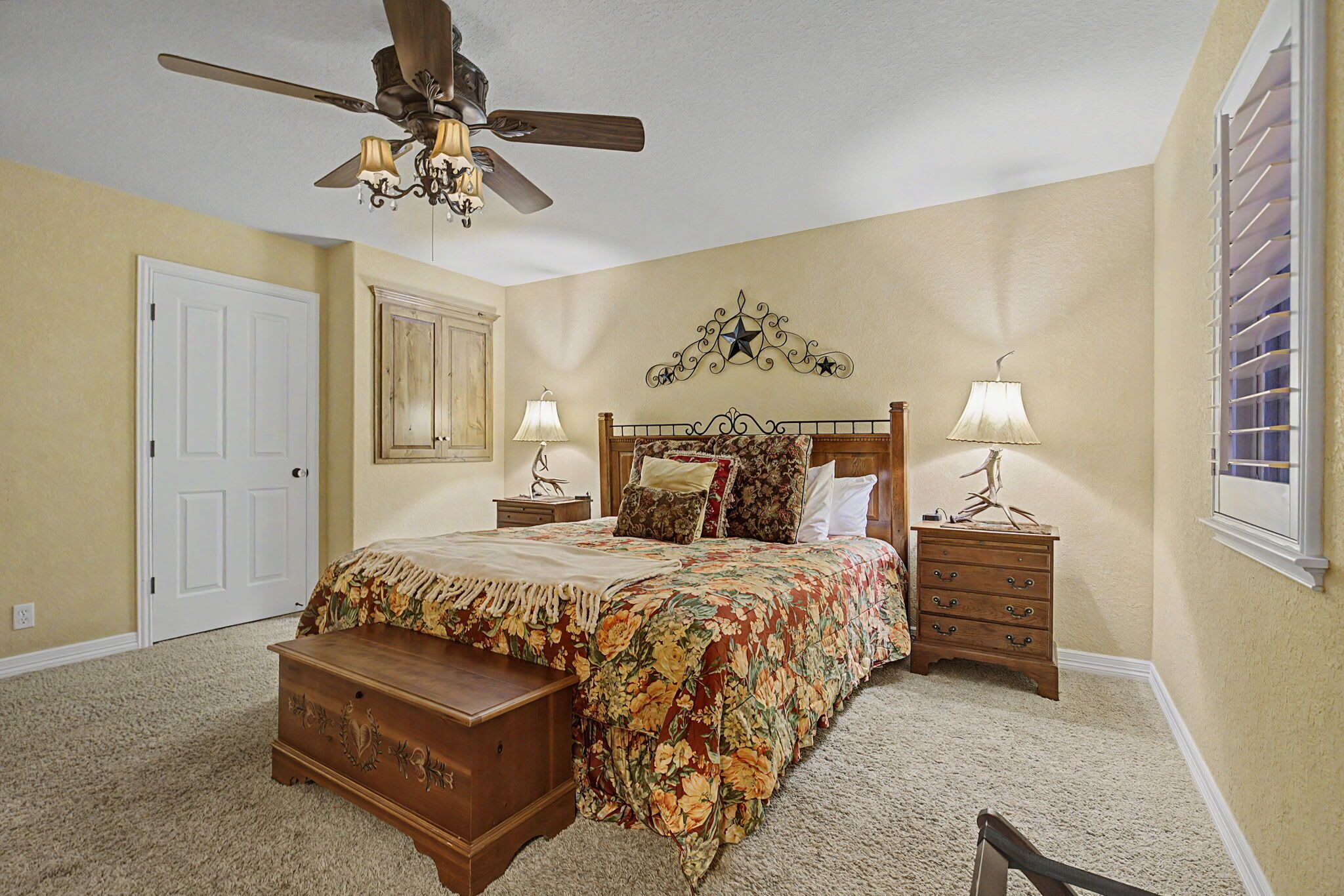 Une chambre à coucher comprenant un lit, une commode, des tables de chevet, un ventilateur de plafond et un élément décoratif mural.