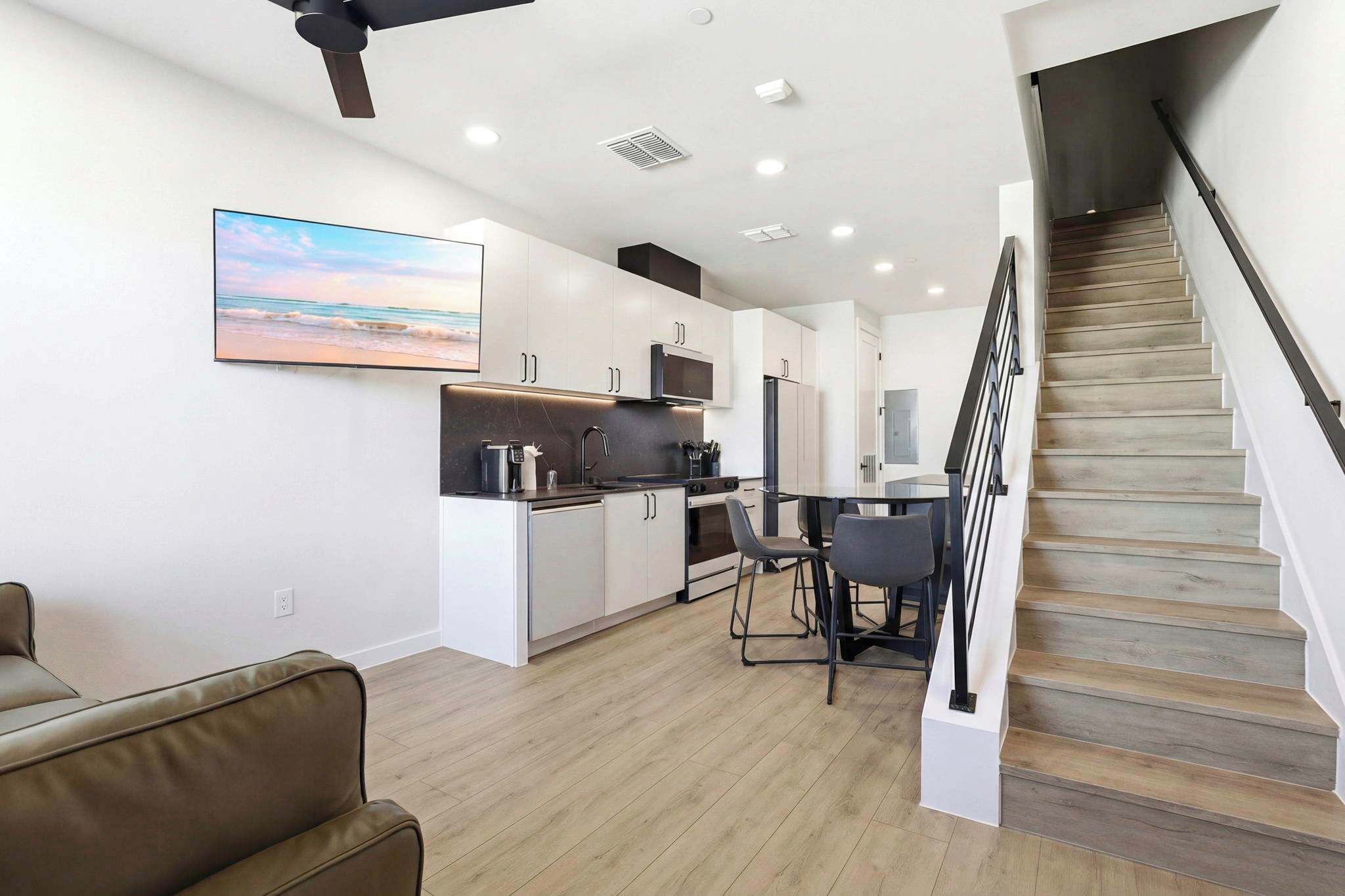 Una cocina moderna con armarios blancos, un comedor con mesa y sillas, y una escalera de madera.