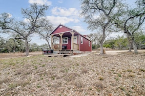 Ein rotes Holzhaus mit Veranda, umgeben von Bäumen und trockenem Gras.