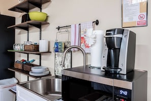 Eine Küchenzeile mit einer Kaffeemaschine, einem Spülbecken und Regalen mit Geschirr.