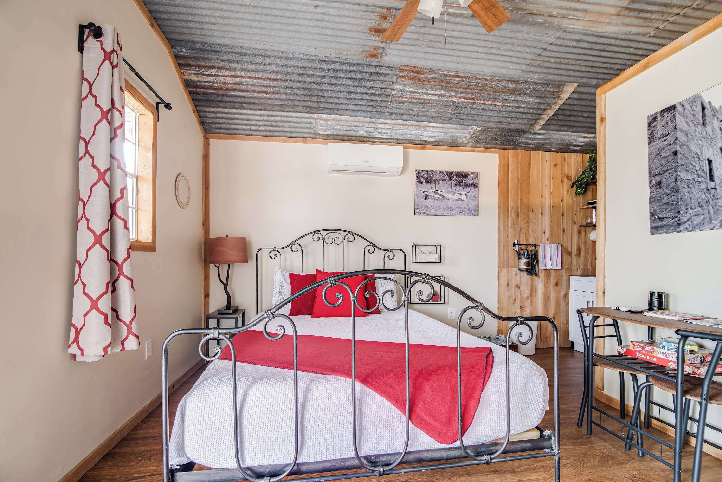 A bedroom with a metal bed frame, a wooden floor, a desk with a chair, and a wooden wall panel.