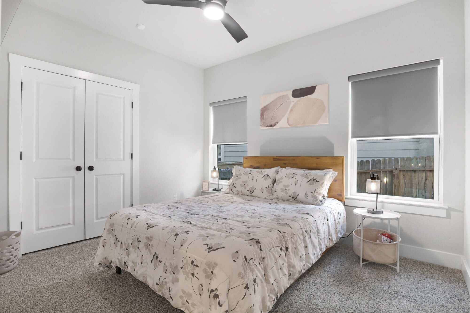 A bedroom with a bed, a ceiling fan, a nightstand, a lamp, and a window.