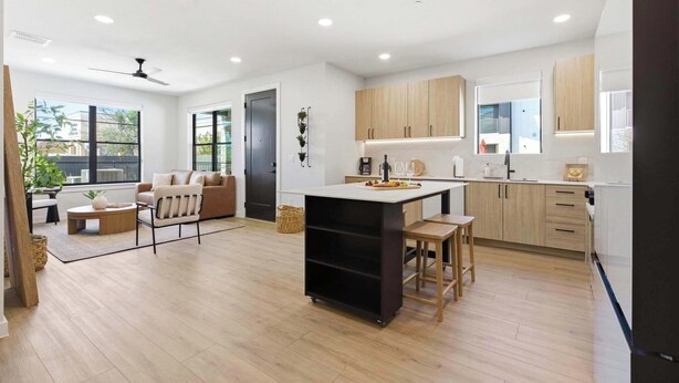 A modern kitchen with wooden cabinets, a central island, and a dining area with a sofa and coffee table. - Unwind in Style: Luxe Condo Getaway! (New Braunfels)