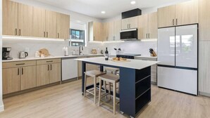 A modern kitchen with wooden cabinets, a central island, bar stools, and a built-in microwave. - Unwind in Style: Luxe Condo Getaway! (New Braunfels)