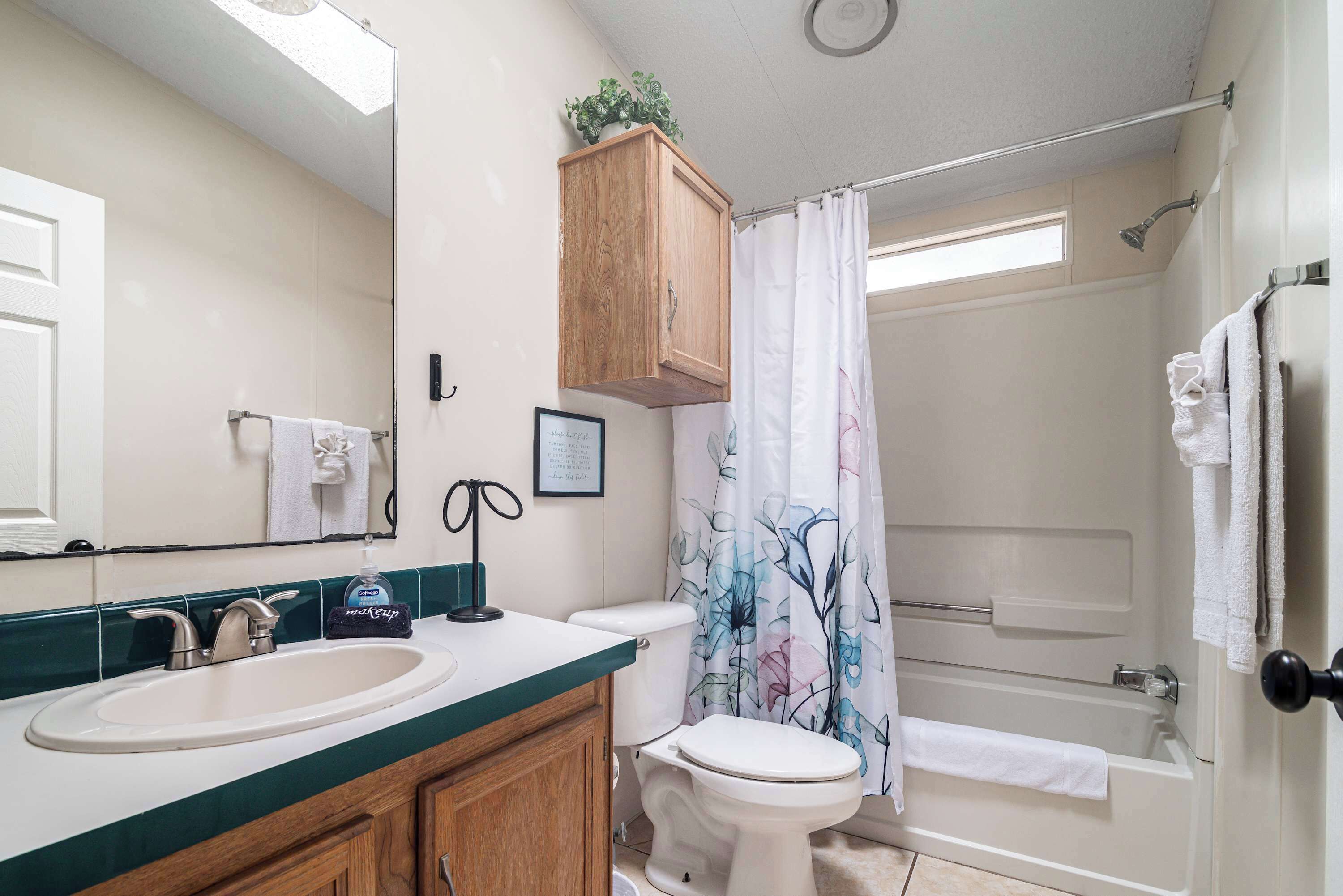 Een badkamer met een wastafel, toilet, douche en een houten kastje boven de wastafel.