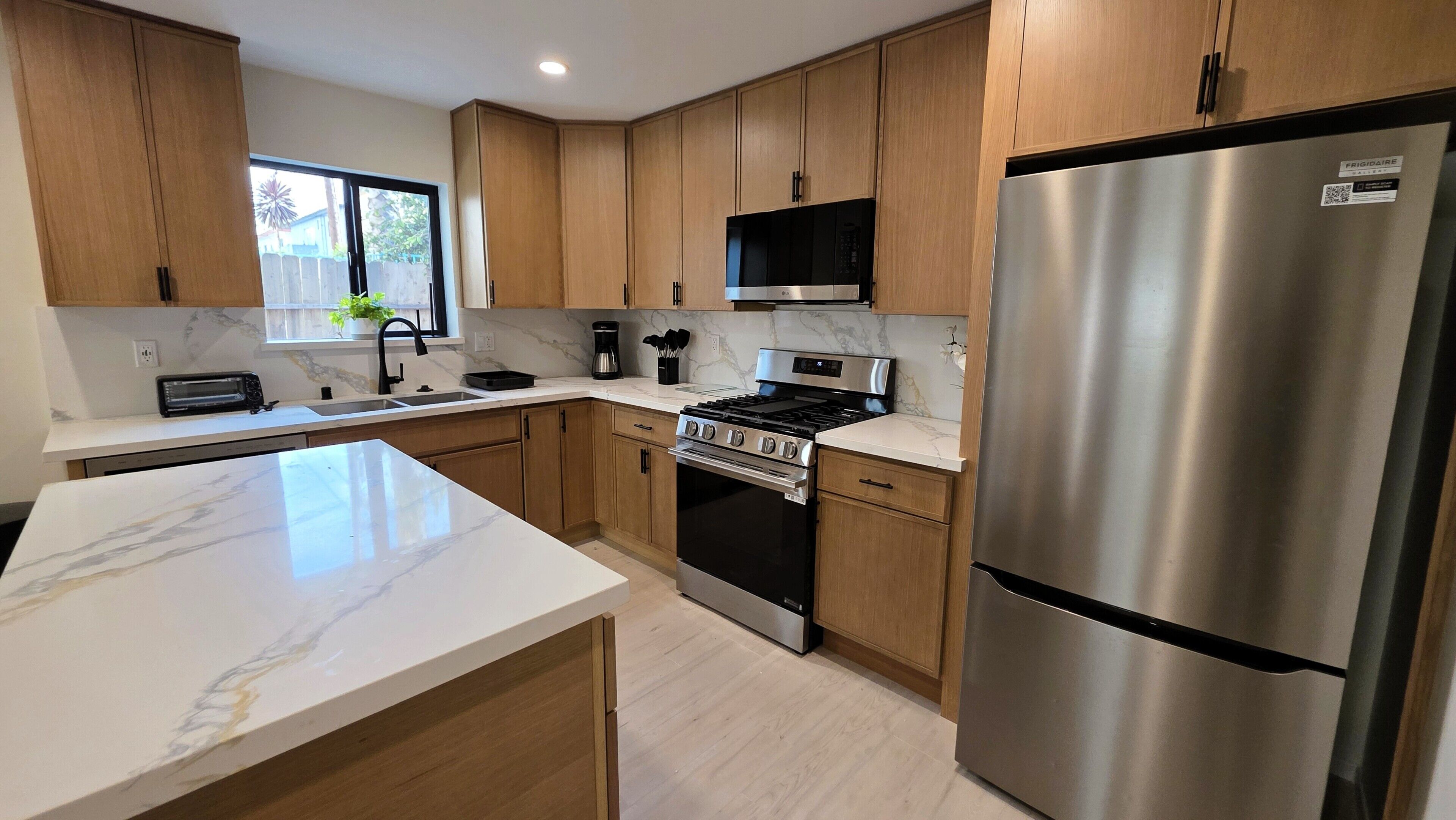 A modern kitchen with wooden cabinets, a stainless steel refrigerator, a built-in oven, and a microwave.