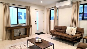 Una sala de estar con sofá, una mesa de centro, chimenea y ventanas grandes con cortinas.