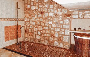 Une salle de bain avec un mur en pierre, un sol carrelé, une douche et un lavabo surmonté d'un panier en osier.