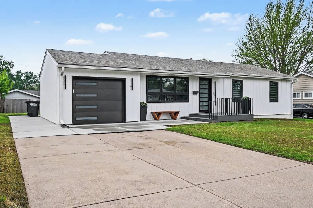 Een modern gelijkvloers huis met garage, een voortuin met bankje en een verzorgd gazon.