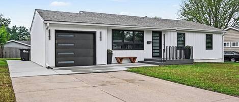 Een modern gelijkvloers huis met garage, een voortuin met bankje en een verzorgd gazon.