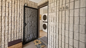 Un pasillo con un papel tapiz decorativo, una puerta con celosía metálica, un banco y el número 236 en la pared.