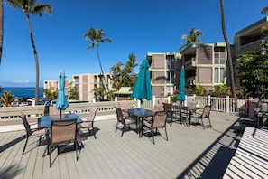 Eine Terrasse im Freien mit Tischen und Stühlen, Palmen und Blick aufs Meer.