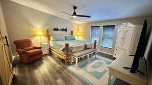 A bedroom with a bed, a chair, a desk, a ceiling fan, and a window with blinds. - Remodeled Cabin in the Heart of Lakeside (Lakeside)