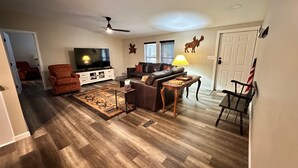 A living room with a television, sofa, armchair, and wooden flooring. - Remodeled Cabin in the Heart of Lakeside (Lakeside)