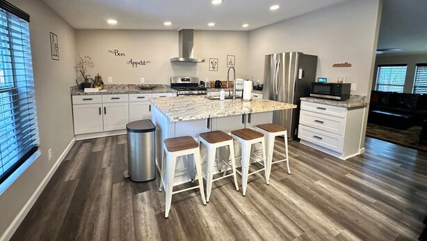 A modern kitchen with a central island, white cabinetry, stainless steel appliances, and a wooden floor. - Remodeled Cabin in the Heart of Lakeside (Lakeside)