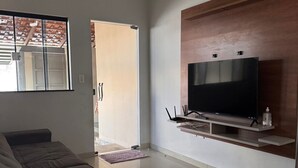 Una sala de estar con sofá, televisor en estante de madera y puerta corrediza de vidrio que da al exterior.