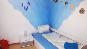 Un dormitorio con una cama individual, una mesita de noche, un atrapasueños colgado en la pared y un pequeño estante con adornos.
