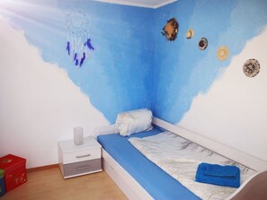 A bedroom with a single bed, a nightstand, a wall-mounted dreamcatcher, and a small shelf with decorative items. - Haus Falke Appartement/Fewo 6-Bettwohnung by Interhome (Saas-Balen)