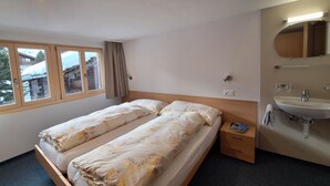 Ein Hotelzimmer mit zwei Betten, einem Fenster mit Vorhängen, einem Badezimmer mit Waschbecken und Spiegel sowie einem kleinen Nachttisch.