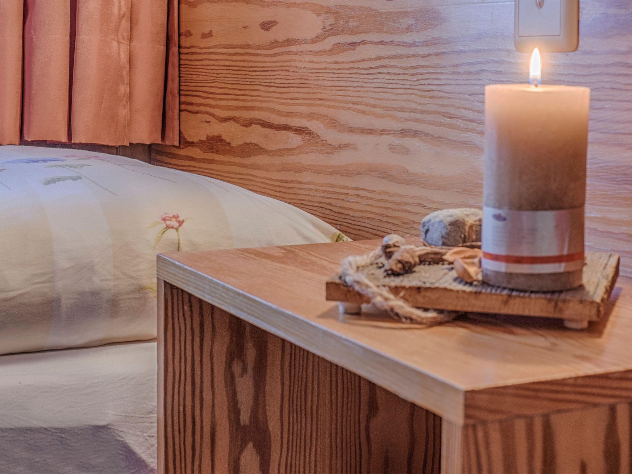 A wooden bedside table with a lit candle, a decorative item, and a pillow with a floral design.