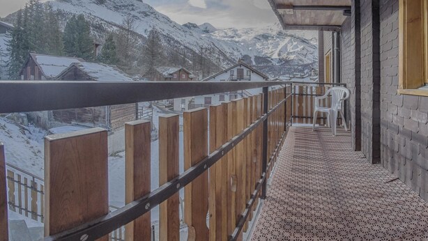 Ein Balkon mit Holzgeländer, einem gemusterten Boden und Blick auf schneebedeckte Berge.
